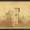 View of people standing on a commercial street, church visible in background.