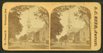View of people standing on a commercial street, church visible in background.