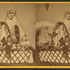 Interior view of a fair or church bazaar showing tables draped with flowers and arranged with items, including a table with photographs and paintings labelled "In Memoriam".