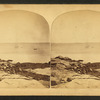 View of a rocky beach with a sail boat in the distance.
