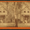 Group gathered on a porch of a large house surrounded by woods.