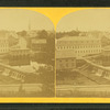 View of town with dam in foreground, churches, homes, other buildings.
