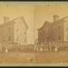 View of unidentified students and teachers in front of wood frame school.