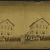 View of unidentified students and teachers in front of wood frame school.]