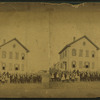 View of unidentified students and teachers in front of wood frame school.