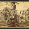 People in front of a wood frame house behind picket fence.