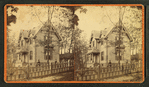 People in front of a wood frame house behind picket fence.