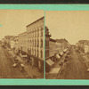 Street scene with buildings, trolley tracks, store fronts, and carriages.