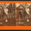 Woman seated at table with fountain, swing, and bench nearby.
