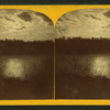 View of moonlight reflecting on water, with trees and clouds.