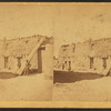 View of an individual standing next to wooden beams that are leaning against an adobe structure.