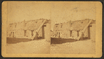 View of an individual standing next to wooden beams that are leaning against an adobe structure.