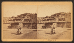 View of two Zuni individuals in front of Pueblo.