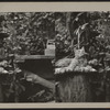 Cat atop pillow on a tree stump.