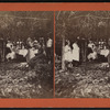 Group eating at table under trees.