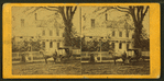 View of a carriage on the street in front of a big house.