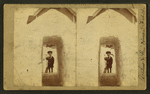 View of a child with a shovel standing behind a tunnel of snow in front of a house.