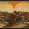 View of a bridge over a river with houses in the background.