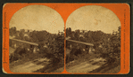 View of a bridge over a river with houses in the background.