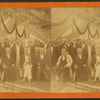 Men seated and standing in festooned tent.