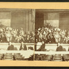 Performers in costume posing on stage with musicians in pit, viewed across orchestra seating.