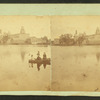 Children in a boat in front of unidentified mill or factory building.
