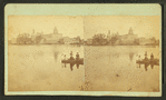 Children in a boat in front of unidentified mill or factory building.