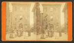 Women and children in front of narrow three story building.