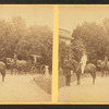 View of African American groom holding reins of horse with rider.
