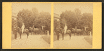 View of African American groom holding reins of horse with rider.