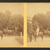 View of African American groom holding reins of horse with rider.