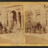 Women boarding a coach and men standing, in front of a house.