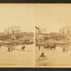 Coaches, horseback rider and people on the beach and houses in the distance.