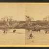 Coaches, horseback rider and people on the beach and houses in the distance.