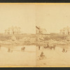 Coaches, horseback rider and people on the beach and houses in the distance.