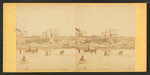 Coaches, horseback rider and people on the beach and houses in the distance.