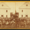 Crowd in front of two story building including women in a carriage and a band.]