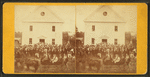 Crowd in front of two story building including women in a carriage and a band.