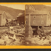 People on rocks near river and buildings damaged by flood.