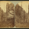 View of a person sitting on a large rock in the mountains.