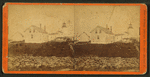 A lighthouse, with rock fence and house in foreground.