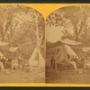 A family sitting under an awning, tents beyond.