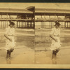 Young woman wading at the beach, in front of a covered pier.