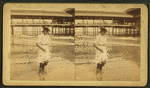 Young woman wading at the beach, in front of a covered pier.