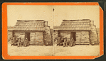 Uncle Ben's cabin. [Elderly couple sitting in front of a cabin.]