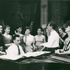 Stephen Sondheim on piano and Leonard Bernstein standing amongst female singers rehearsing for West Side Story (variant).