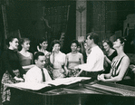 Stephen Sondheim on piano and Leonard Bernstein standing amongst female singers rehearsing for West Side Story (variant).