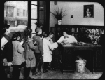 Chatham Square Branch, children lined up at librarian's desk, April 11, 1910; "The Night Library"