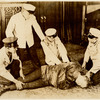 Harry Houdini on floor in straight jacket, surrounded by four unidentified men in white jackets and caps