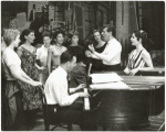 Stephen Sondheim on piano with Leonard Bernstein and Carol Lawrence (on far right) standing amongst female singers rehearsing for the stage production West Side Story.